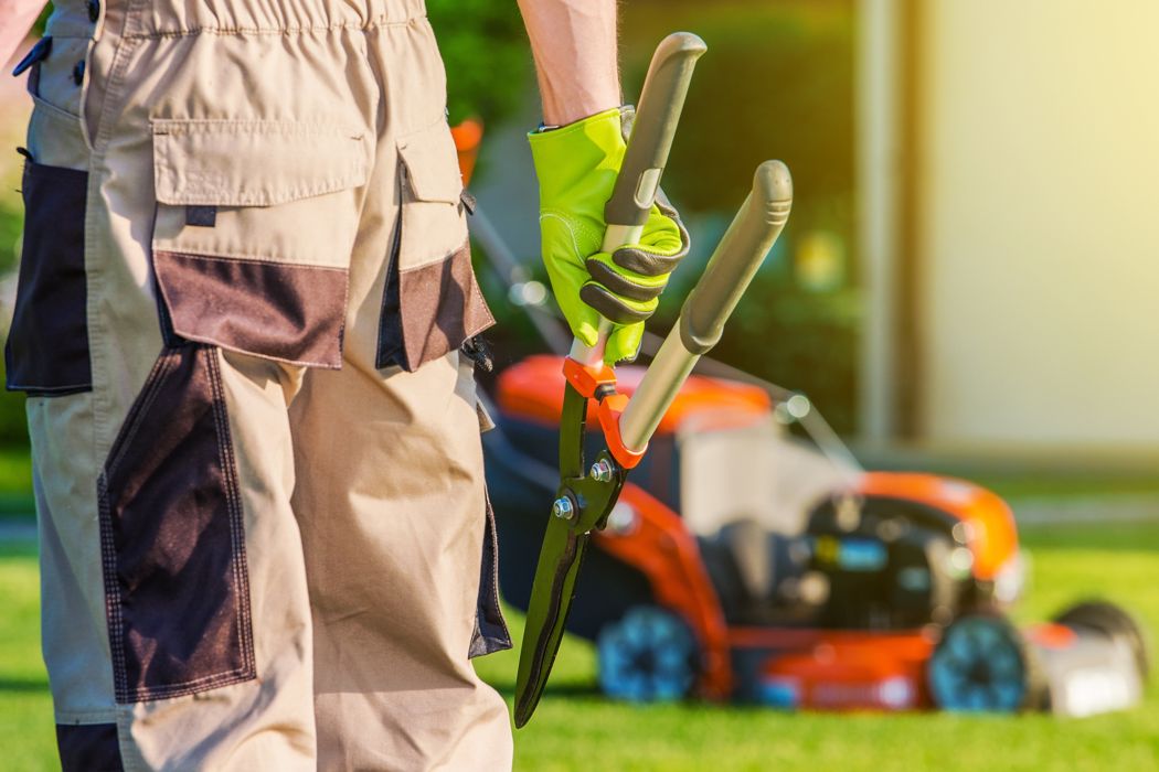 Professional landscaper holding large scissors near an orange lawn mower