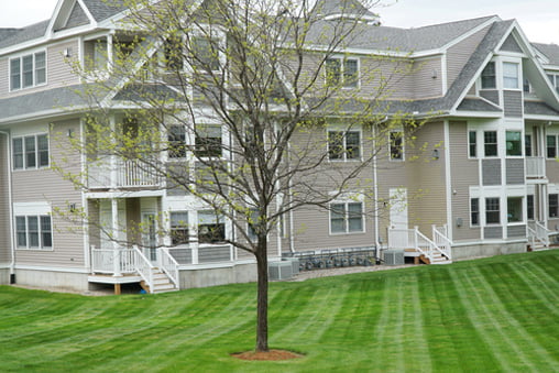 apartment building with mowed green lawn and tree